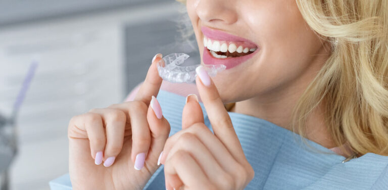 woman smiling while holding a clear aligner close to her mouth