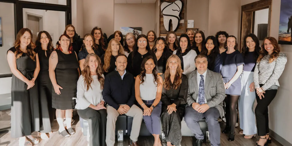 ThoroughDent Smiles group photo taken in a professional office setting, featuring individuals in formal attire with dental-themed artwork and modern decor in the background.